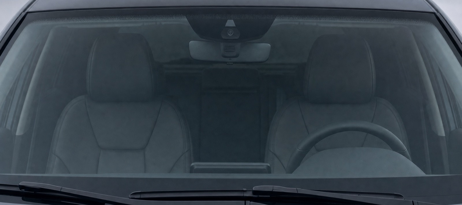 A car windshield photographed square on from outside the vehicle, wipers at the bottom and the camera housing behind the rear view mirror.